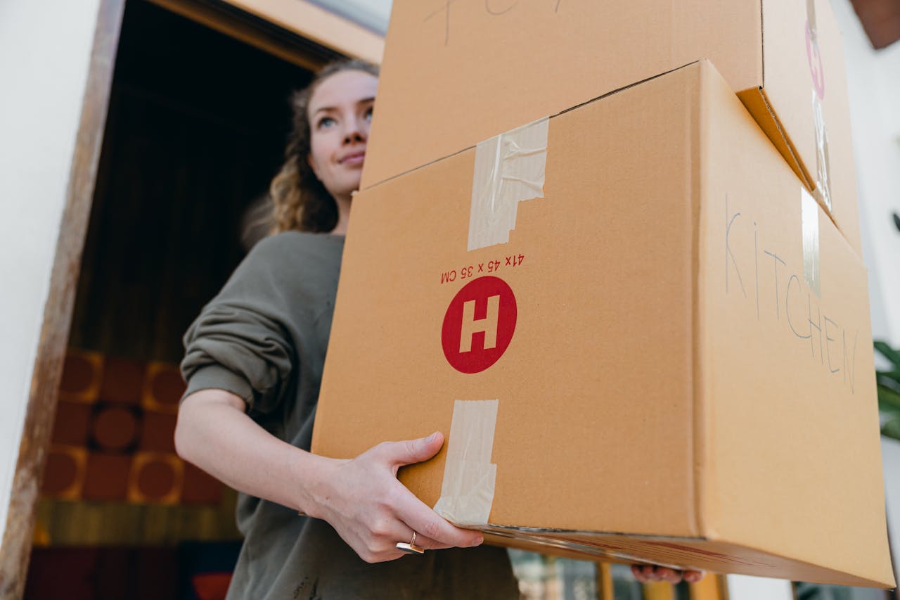 Young female carrying cardboard boxes while moving out of house